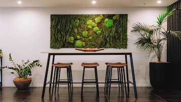Un interior moderno con piso de madera oscura, una mesa con tres taburetes, una obra de arte grande en la pared y plantas en macetas.