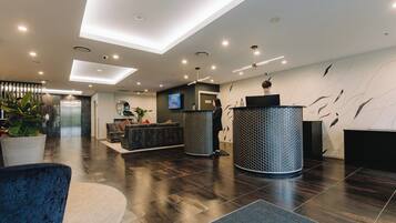 A modern lobby with a reception desk, seating area, and a large potted plant.