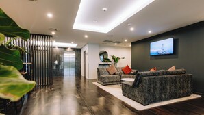A modern lobby with dark wood flooring, a sofa set, a flat-screen TV, and a plant. - Ramada by Wyndham Newmarket Auckland (Auckland)