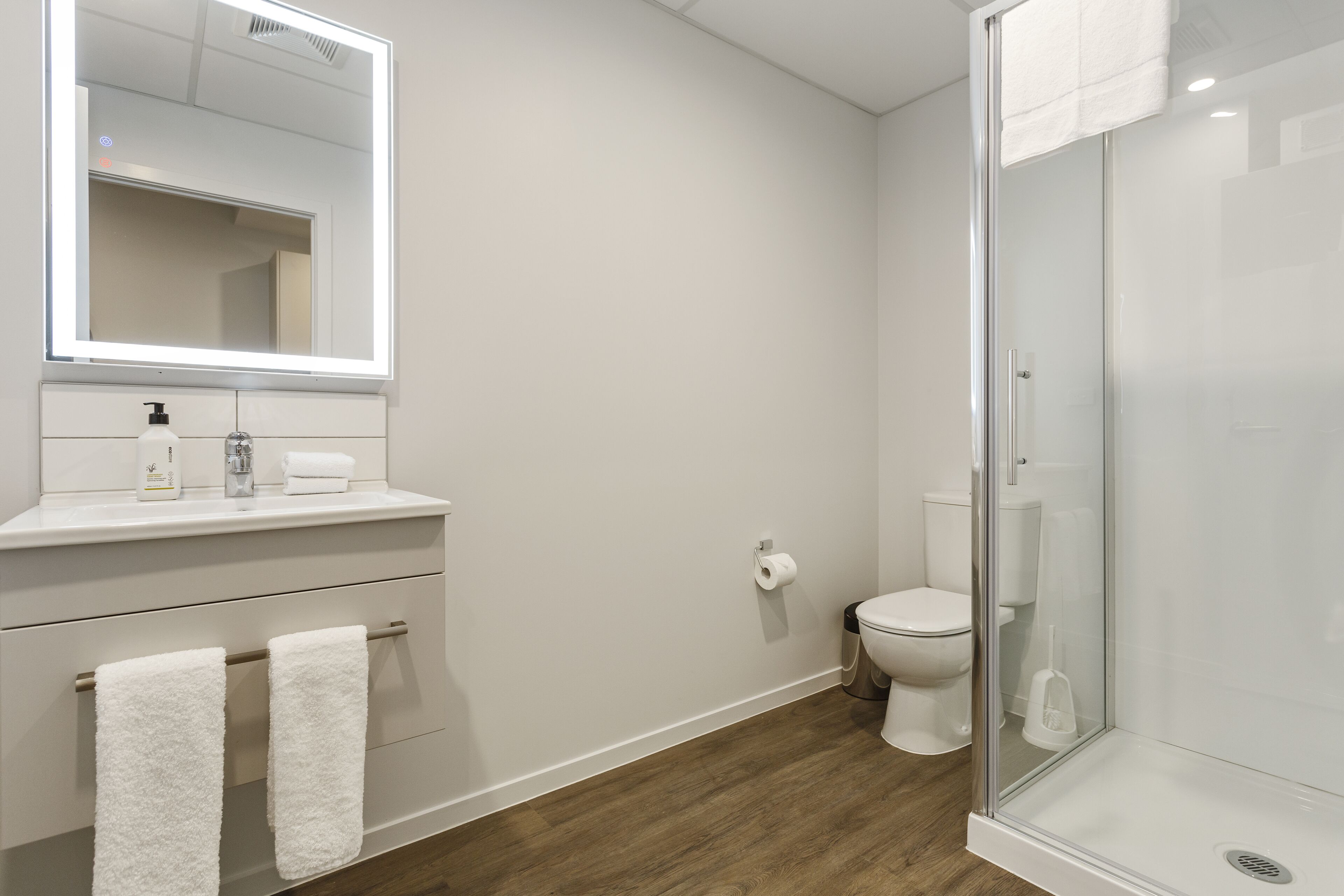 Un baño moderno con cabina de ducha de vidrio, inodoro blanco y tocador con espejo y perchero.