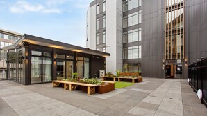A modern building with large windows, a courtyard with benches and planters, and a paved walkway. - Ramada by Wyndham Newmarket Auckland (Auckland)