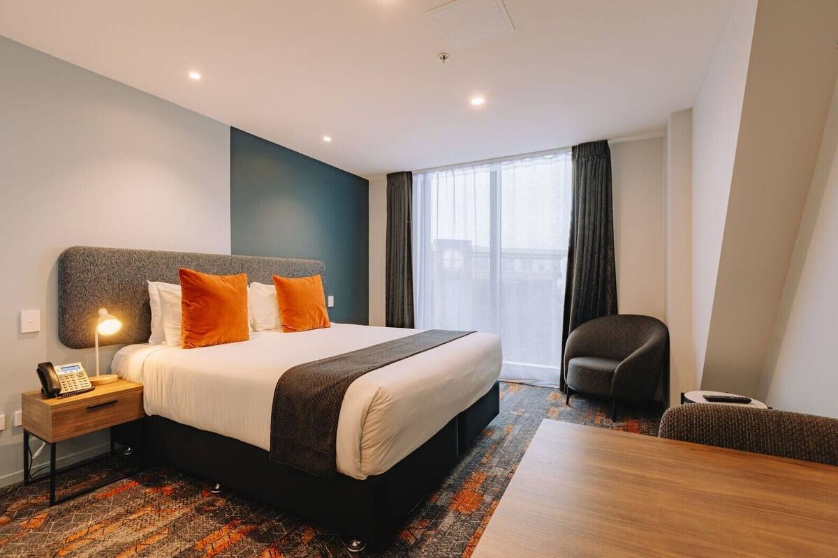 Une chambre d’hôtel avec un grand lit, un bureau avec une lampe, une chaise et une vue sur l’extérieur.