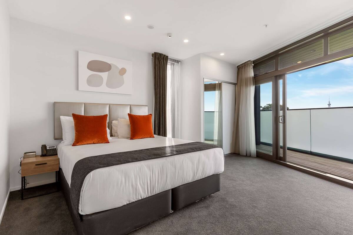 Une chambre d’hôtel moderne avec un grand lit, une table de chevet, une commode, une fenêtre avec des rideaux et une vue sur la ville.