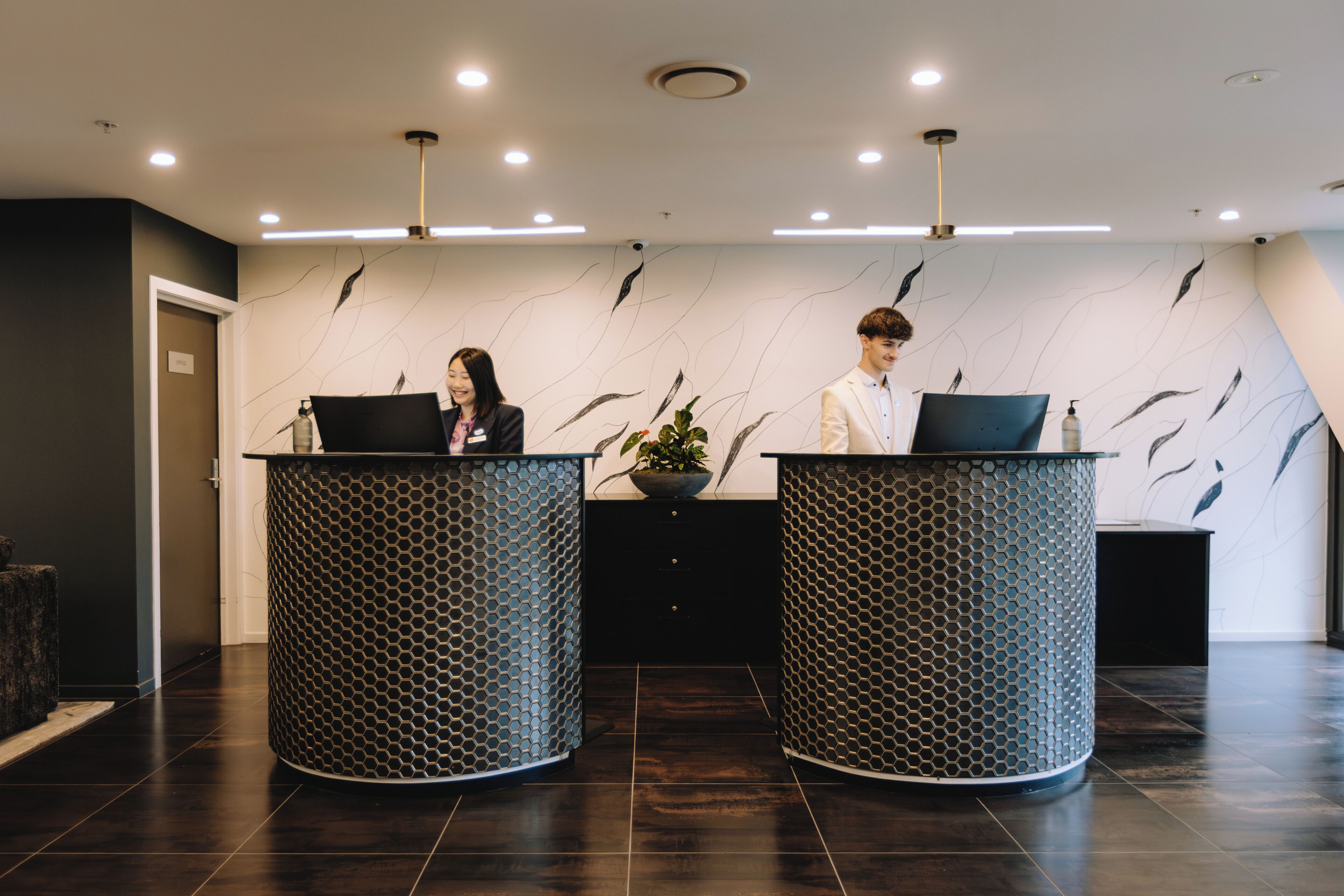 Two reception counters with a modern design, a patterned wall, and a dark floor.