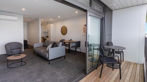 A modern living room with a grey sofa, armchairs, a small round table, and a glass door leading to an outdoor area with a wooden deck. - Ramada by Wyndham Newmarket Auckland (Auckland)