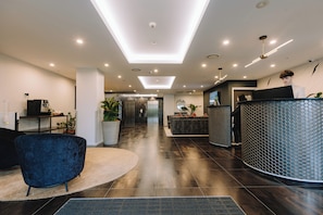 A modern reception area with a reception desk, seating, potted plants, and a dark wood floor.