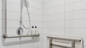 A modern bathroom with white tiled walls, a shower with a handheld showerhead, and a grab bar.