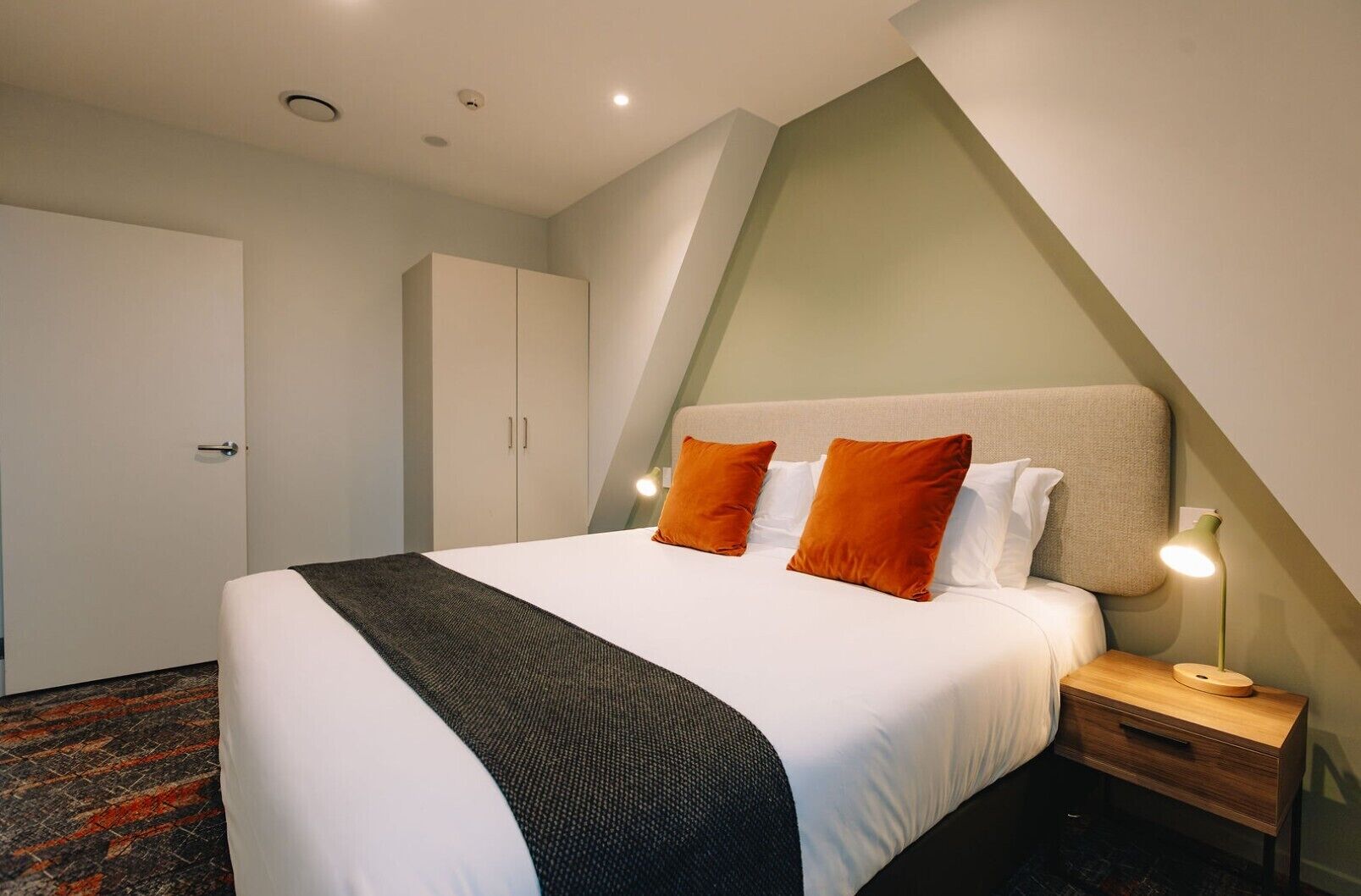 Una habitación de hotel ordenada con cama, mesita de noche y armario.