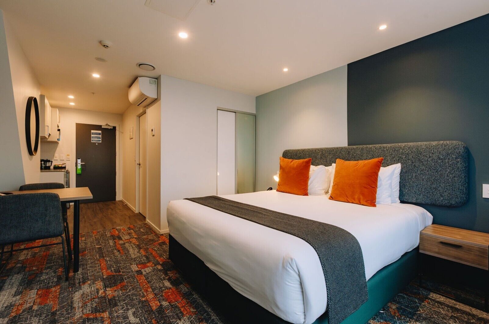 Ein Hotelzimmer mit Bett, Schreibtisch, Stuhl, Kleiderschrank und einer Küchenzeile.