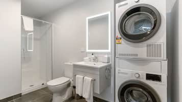 Un baño moderno con ducha envuelta en vidrio, un inodoro, un lavamanos con espejo y una lavadora y secadora apiladas.