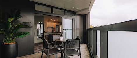 A balcony with a table and chairs, a potted plant, and a view of the interior.