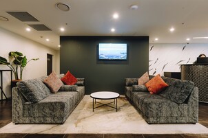 Un salon moderne avec deux canapés gris, une table basse ronde et un téléviseur à écran plat fixé au mur.