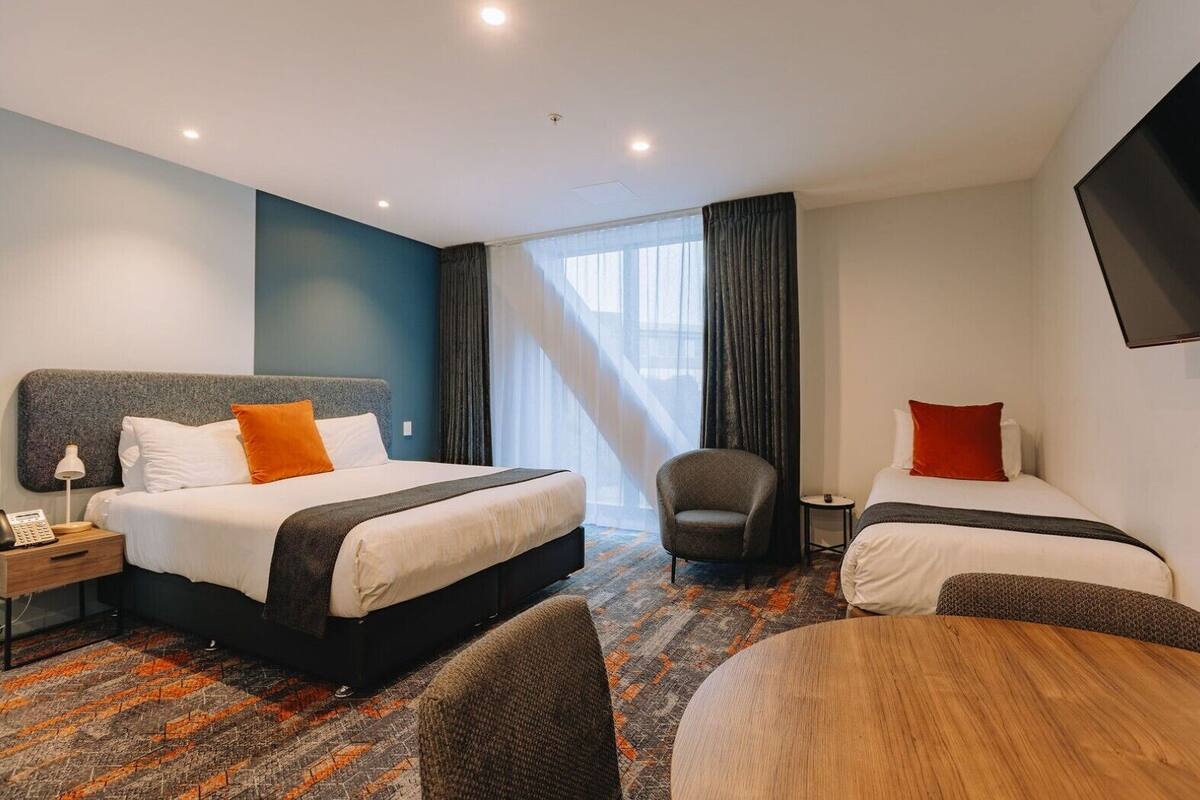 Une chambre d’hôtel avec deux lits, un bureau, une chaise, une télévision et une grande fenêtre.