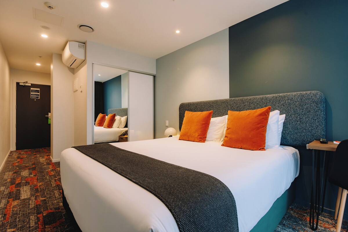 Une chambre d’hôtel avec un grand lit, un bureau, une chaise, un appareil de climatisation et un miroir.