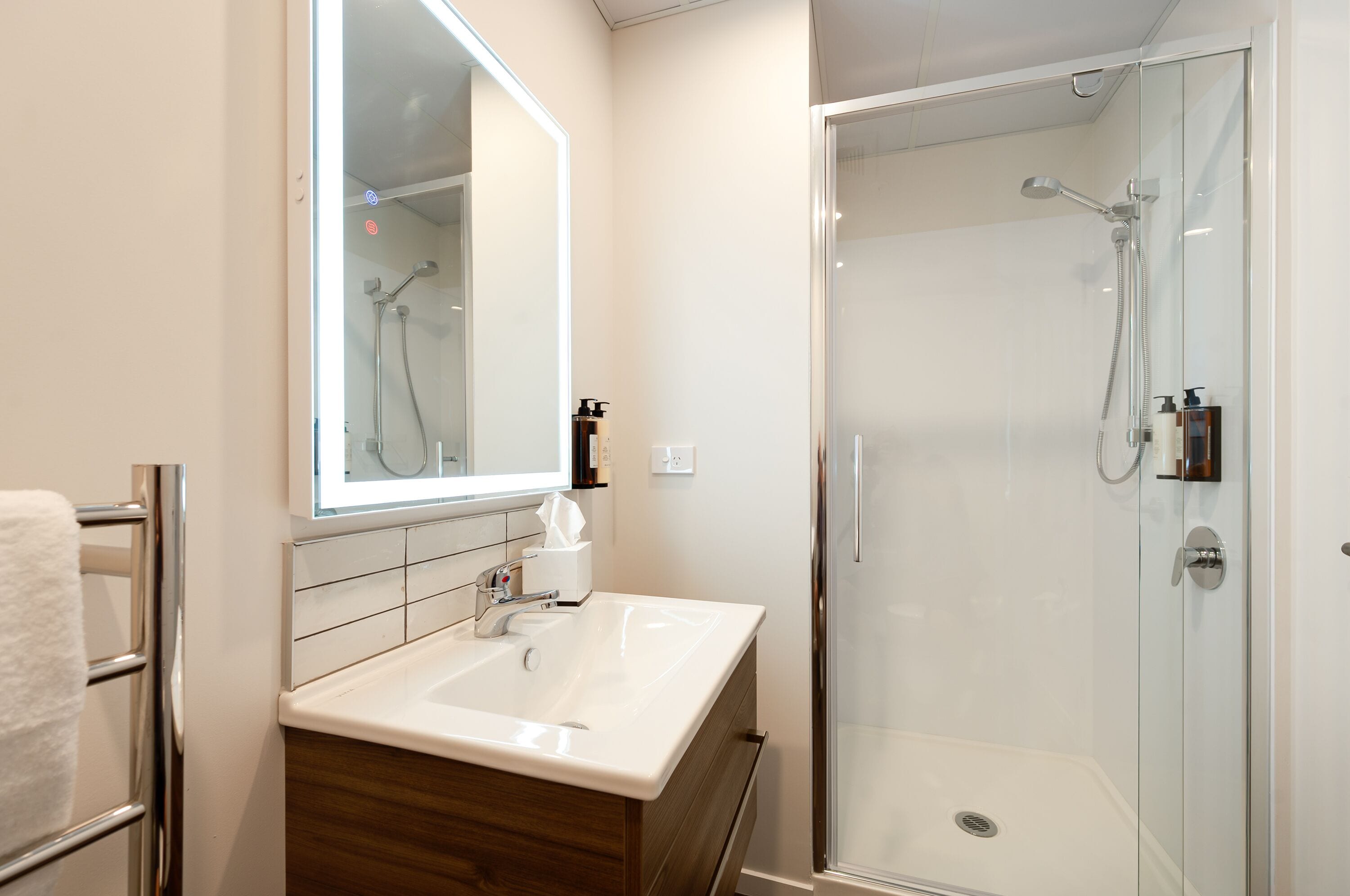 A modern bathroom with a large mirror, a sink, and a glass-enclosed shower.
