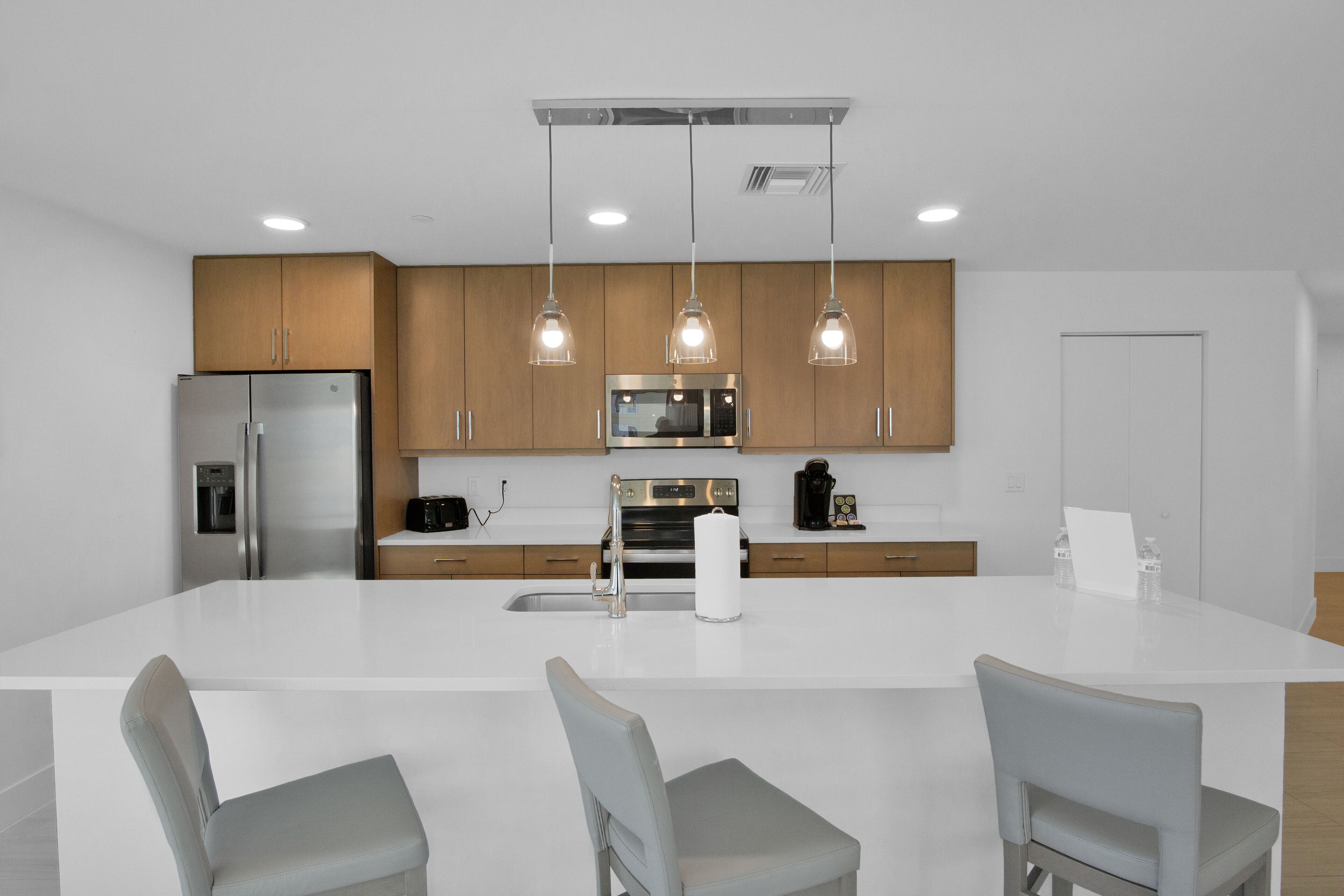 Una cocina moderna con una isla central, electrodomésticos de acero inoxidable, armarios de madera e iluminación colgante.