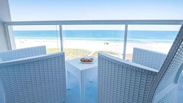 A balcony with wicker furniture overlooking a beach.