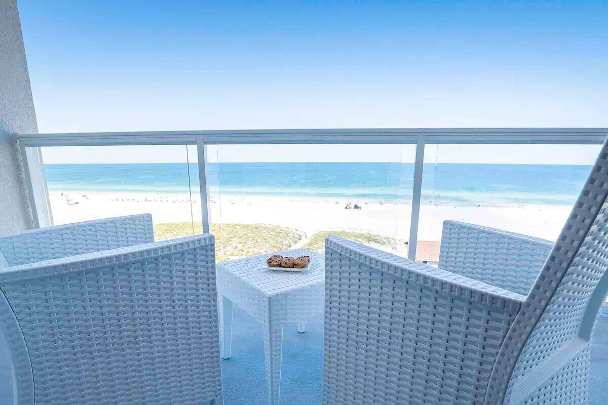 A balcony with wicker furniture overlooking a beach.