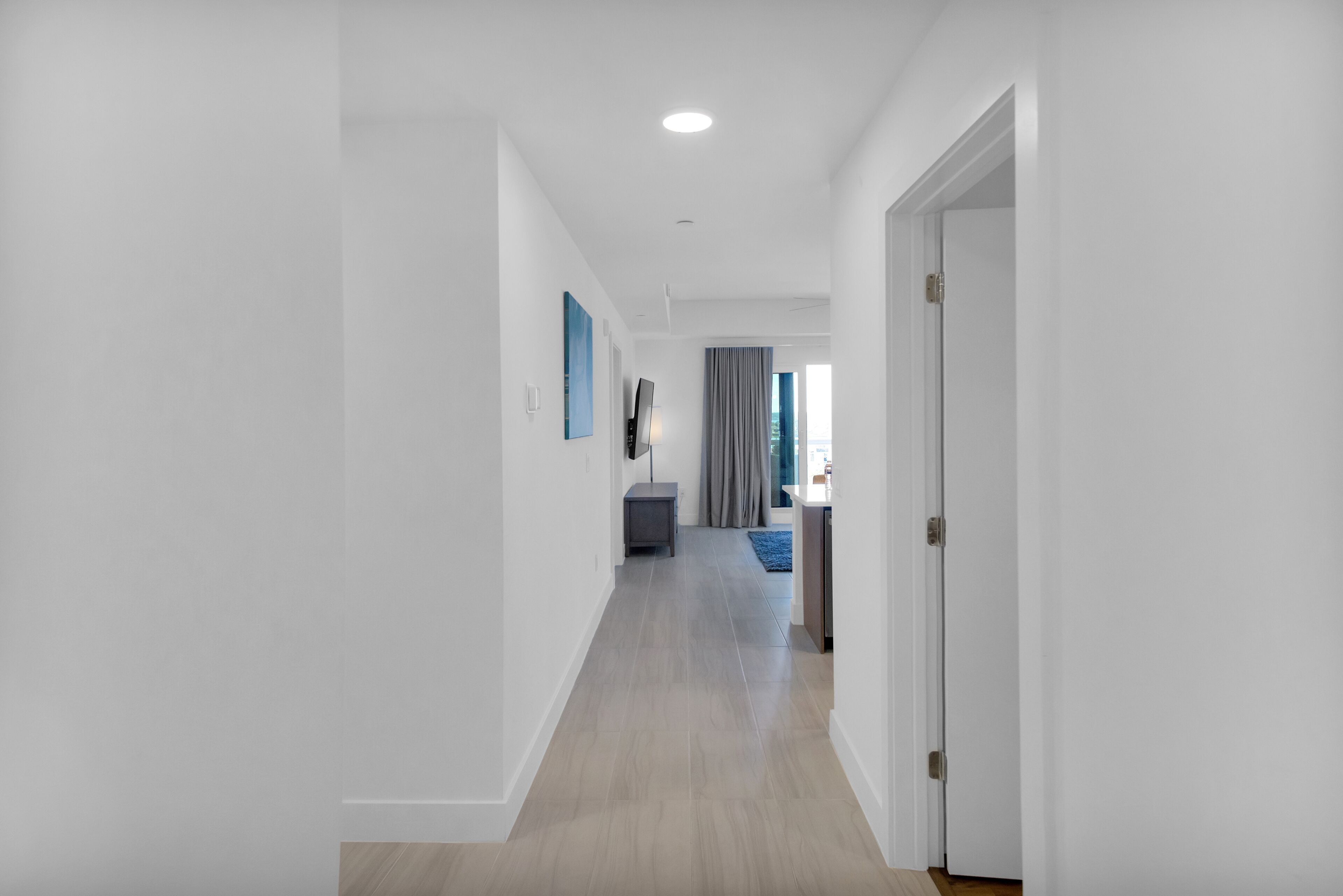 A modern hallway with a wooden floor, white walls, and a door leading to a bedroom.