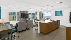 A modern hotel room with a dining area, a kitchen, and large windows offering a view of the city.