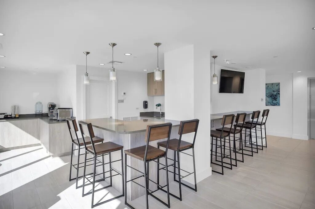A modern kitchen with a central island, bar stools, pendant lighting, and a flat-screen TV on the wall.