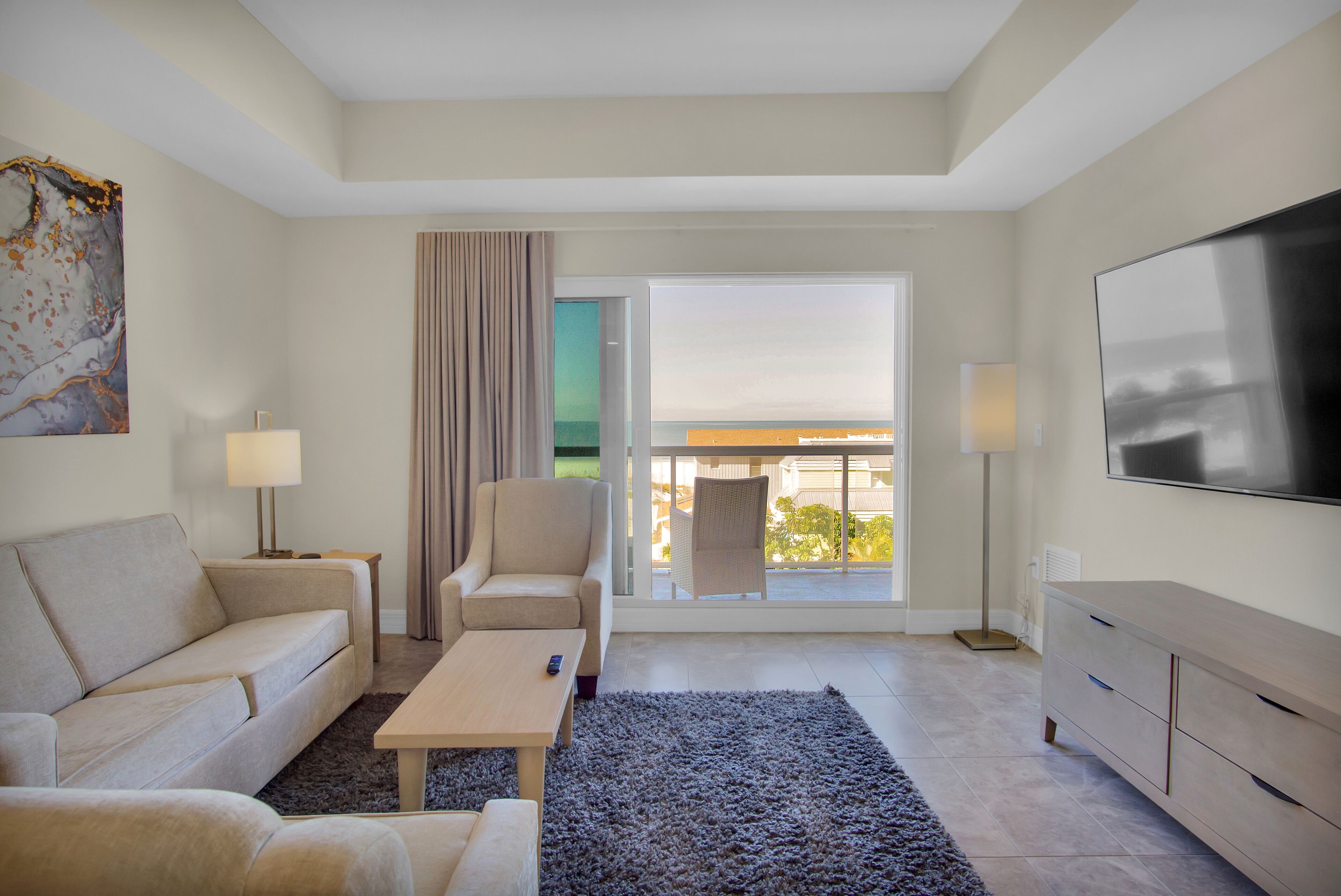 Una habitación de hotel moderna con sofá, sillón, mesa de centro y televisión.