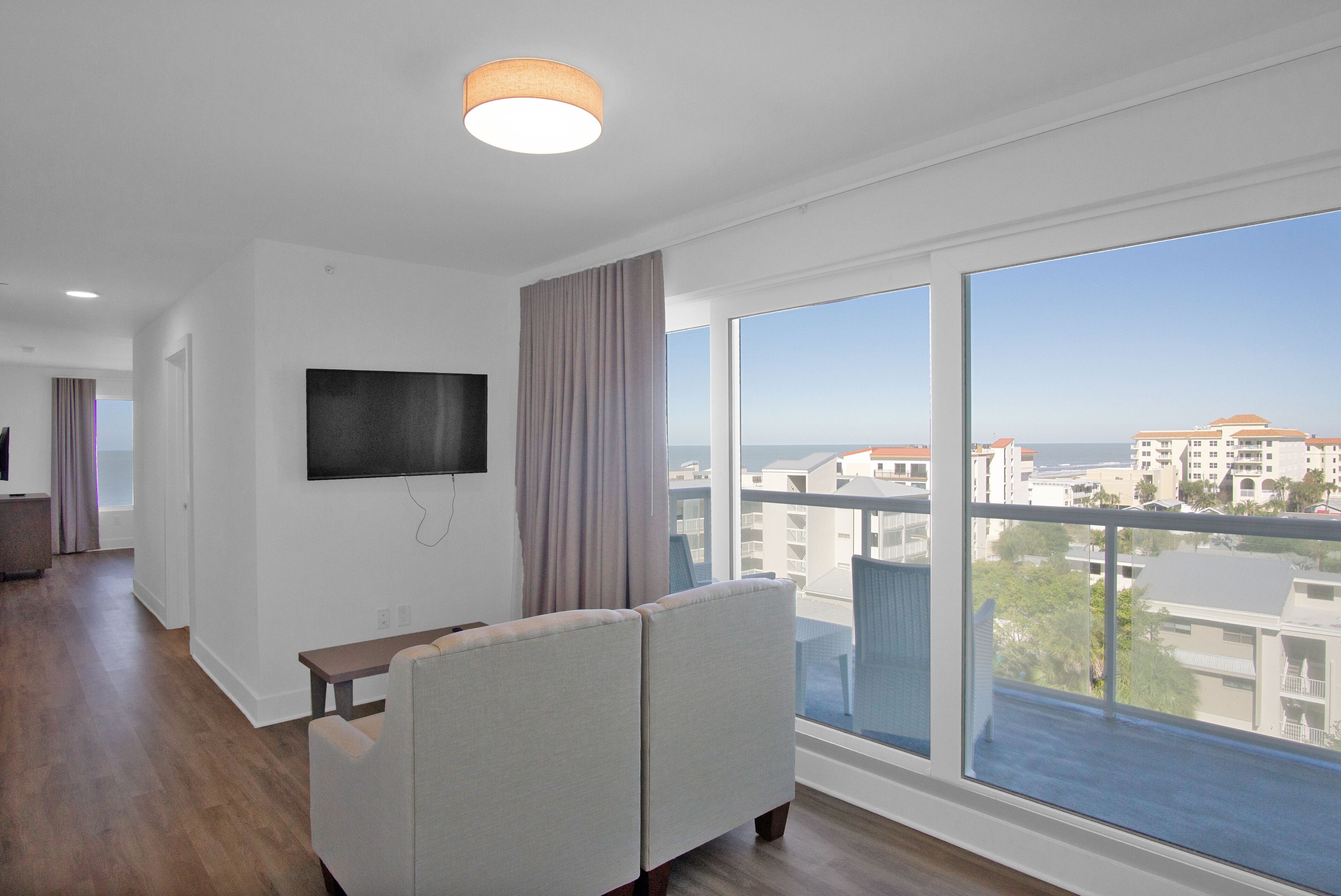 Een moderne woonkamer met een groot raam, een flatscreen televisie aan de wand en een bank.