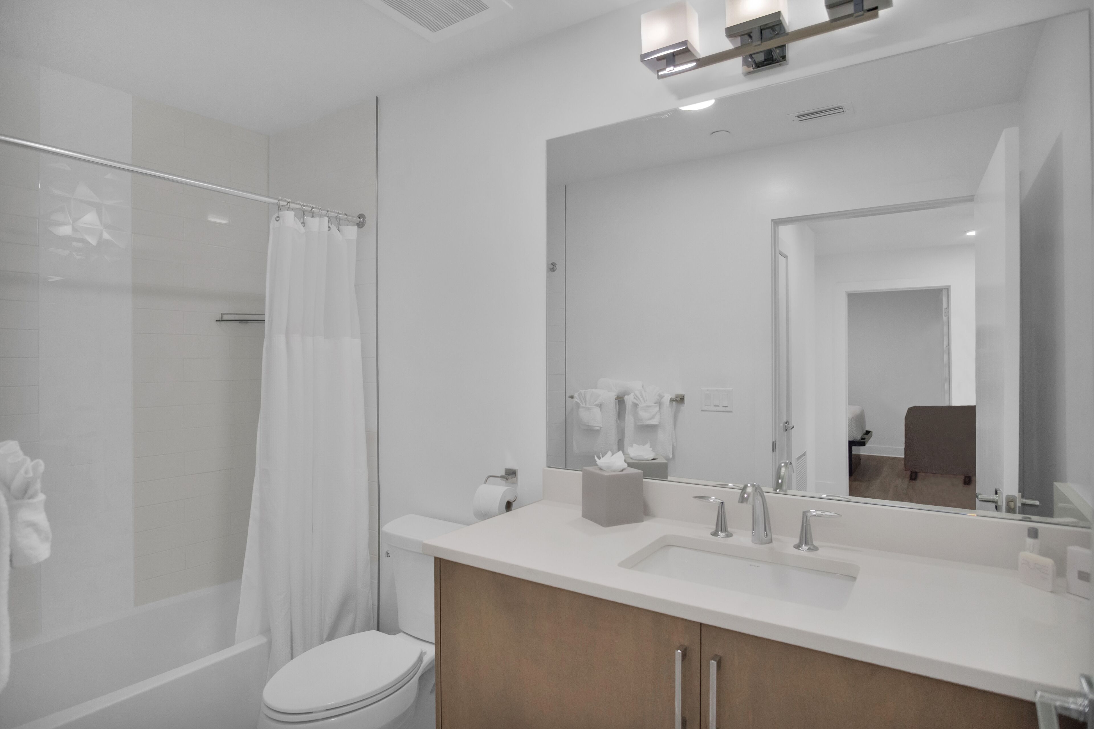 A modern bathroom with a glass shower enclosure, a white toilet, and a large mirror above a sink with a wooden cabinet below.