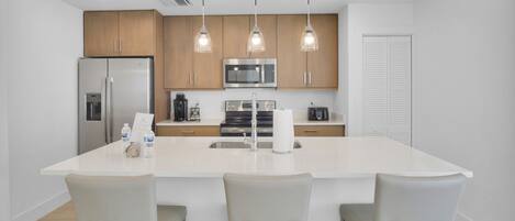 A modern kitchen with a central island, stainless steel appliances, and pendant lighting.