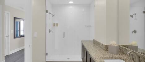 A modern bathroom with a walk-in shower, a vanity with a sink, and a large mirror.