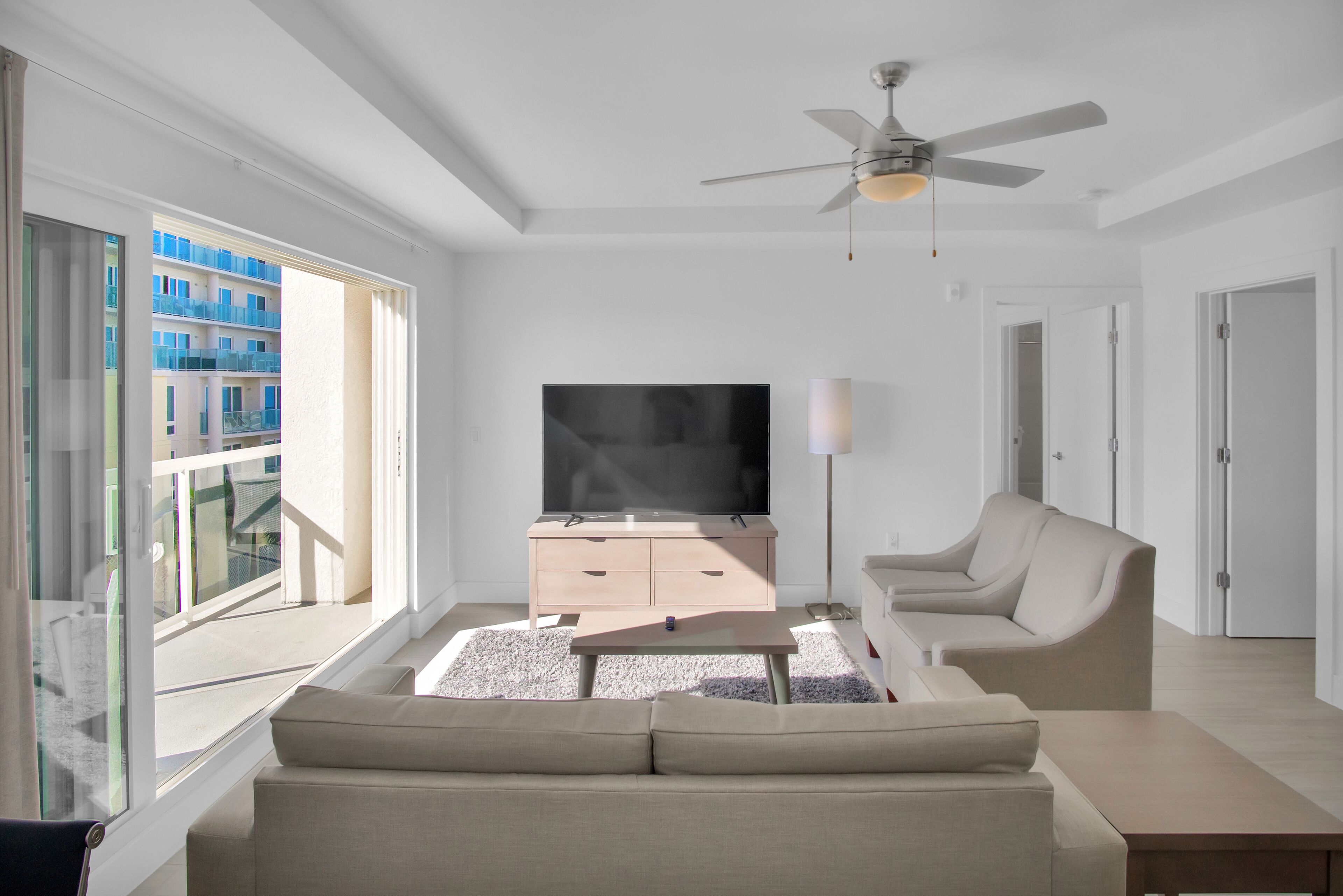 A modern living room with a large TV, a sofa, a coffee table, and a ceiling fan.