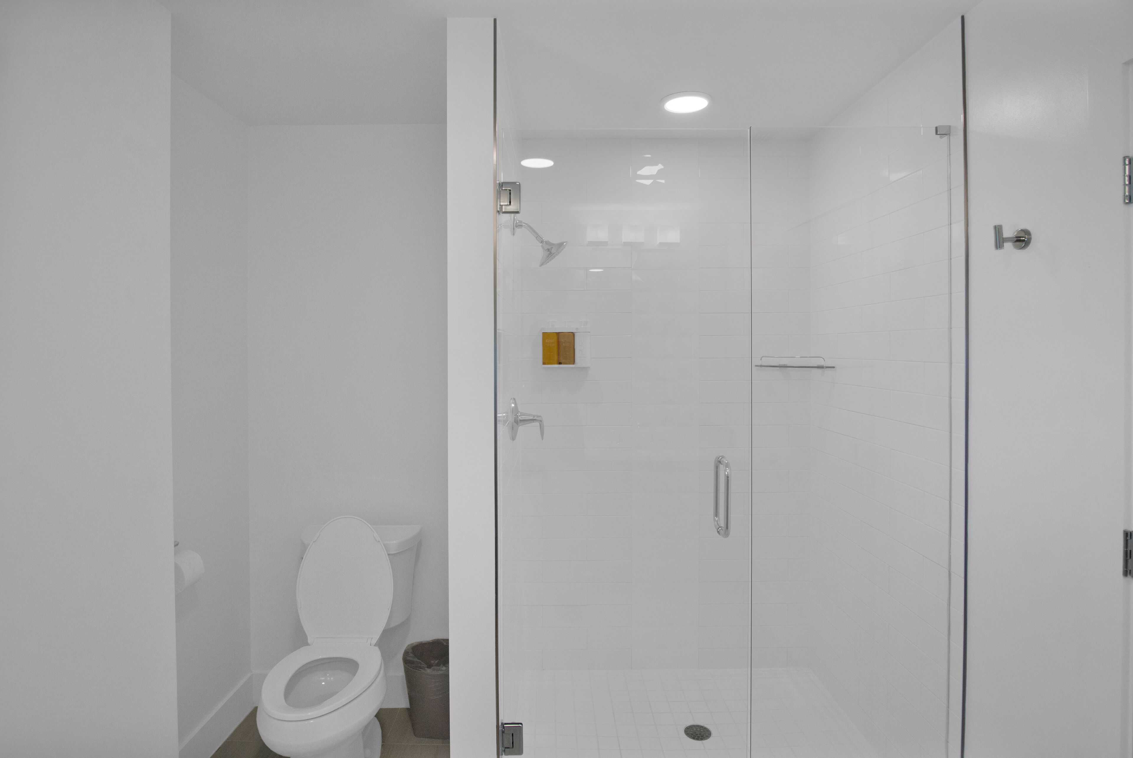 Casa de banho moderna com sanita, zona de duche com parede de vidro e parede revestida a mosaico branco.