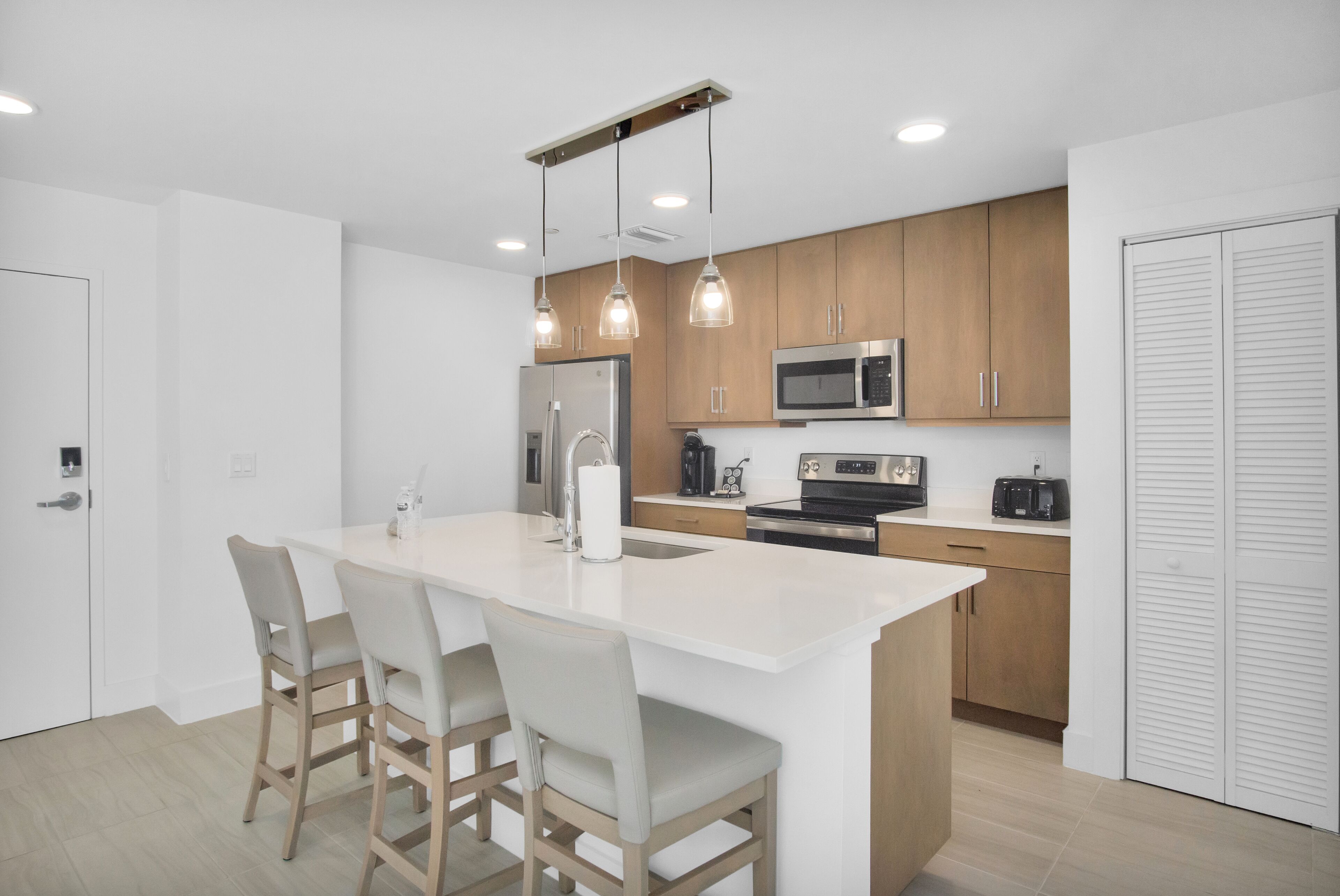 A modern kitchen with a central island, wooden cabinets, stainless steel appliances, and pendant lighting.