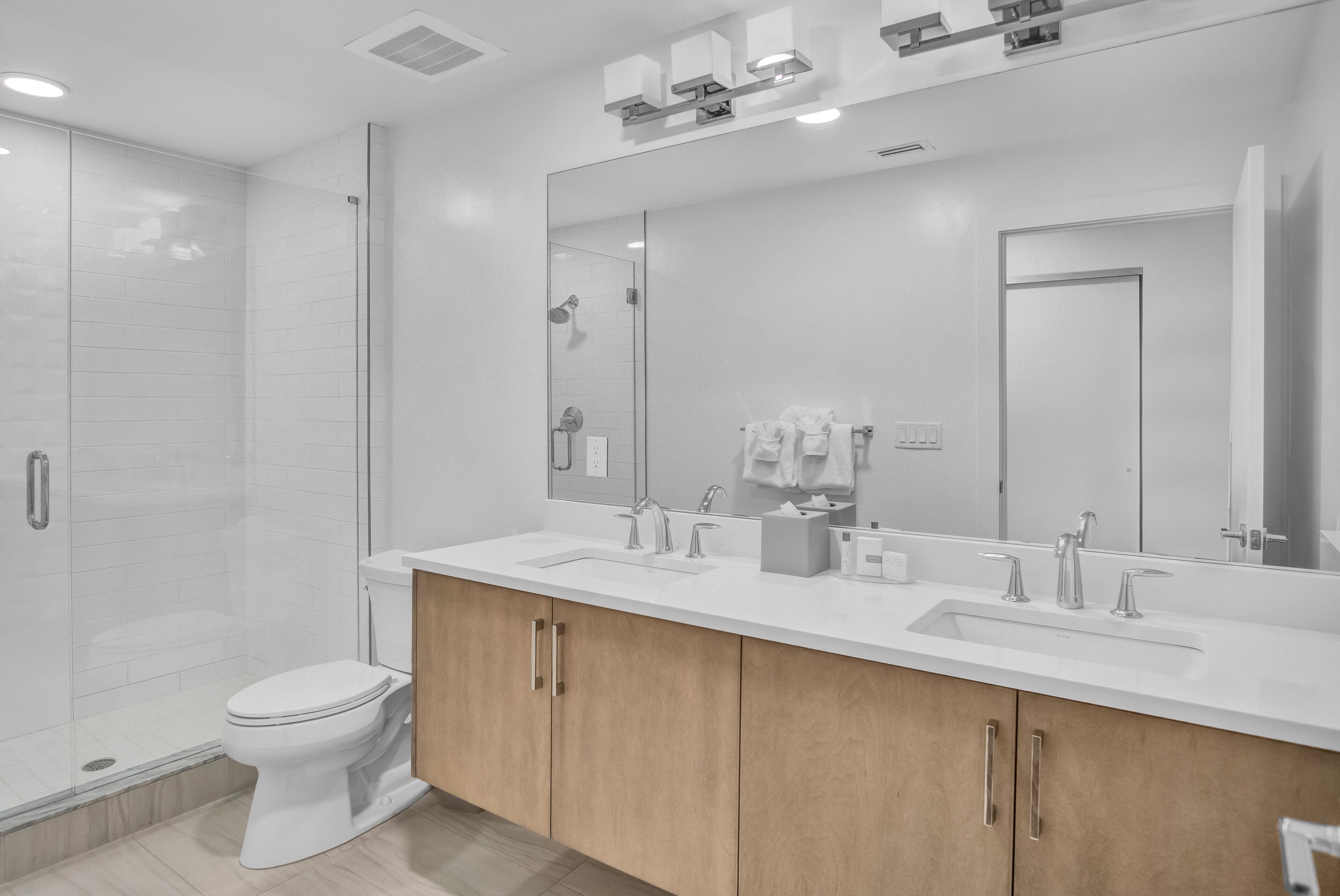 A modern bathroom with a glass-enclosed shower, a white toilet, and a double sink vanity with wooden cabinets.