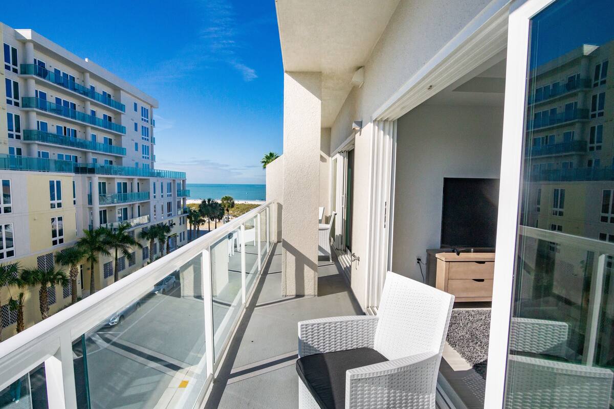 A balcony with a view of the ocean, white wicker furniture, and a wooden cabinet.