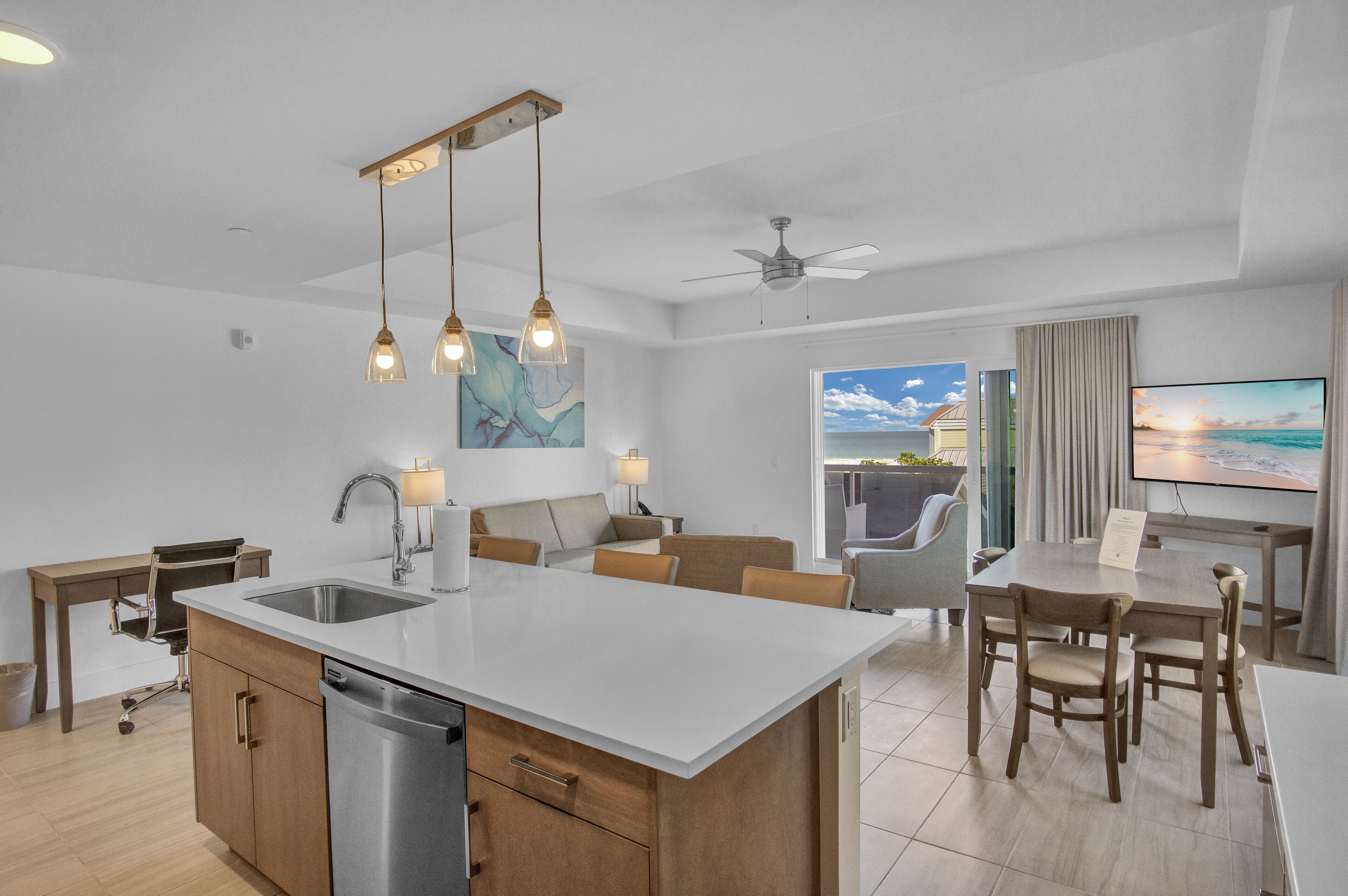 A modern kitchen with a central island, dining area with wooden chairs, and a large flat-screen TV.