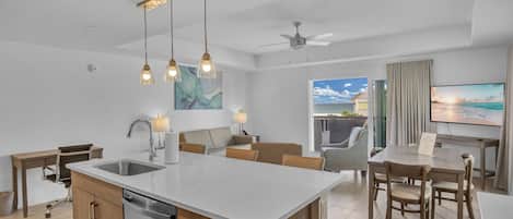A modern kitchen with a central island, dining area with wooden chairs, and a large flat-screen TV.