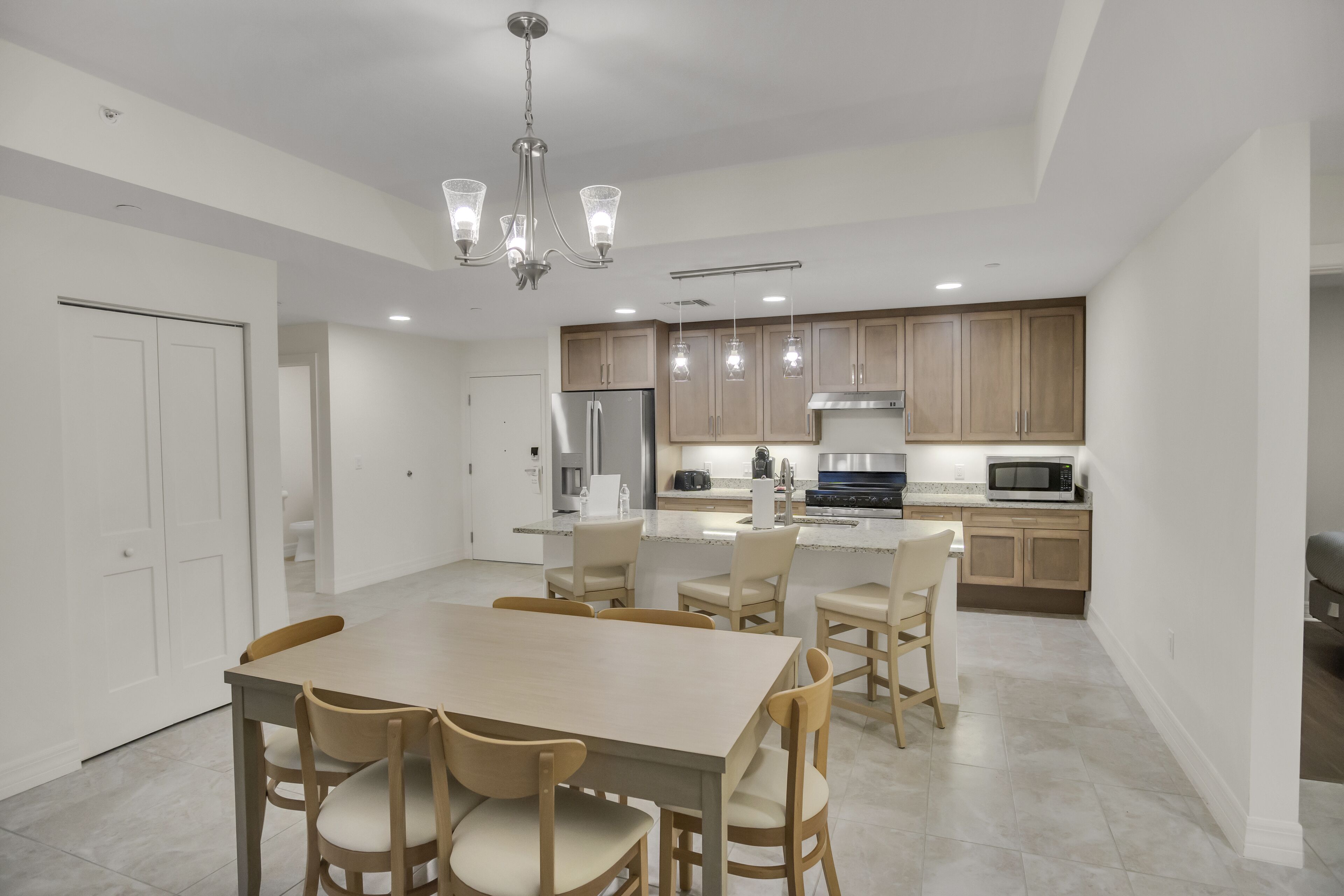 A modern kitchen with wooden cabinets, a central island, and a dining area with a table and chairs.
