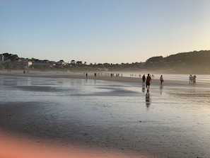 A beach with people walking, a clear sky, and buildings in the background.