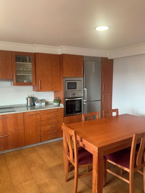 A kitchen with wooden cabinets, a stainless steel refrigerator, a microwave, and a dining table with chairs.
