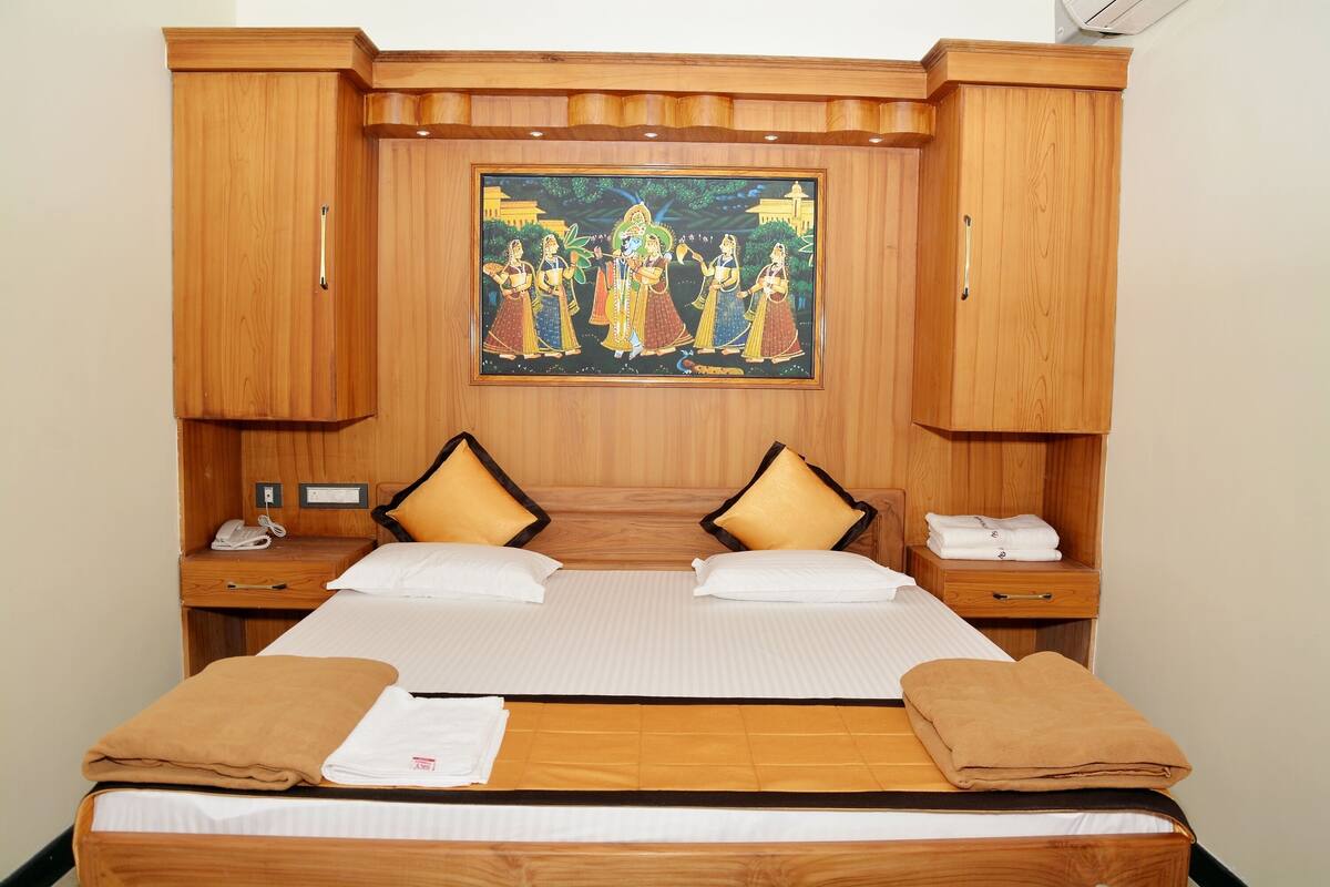 A hotel room with a large bed, two bedside tables, a wooden headboard with a painting, and matching wooden cabinets.
