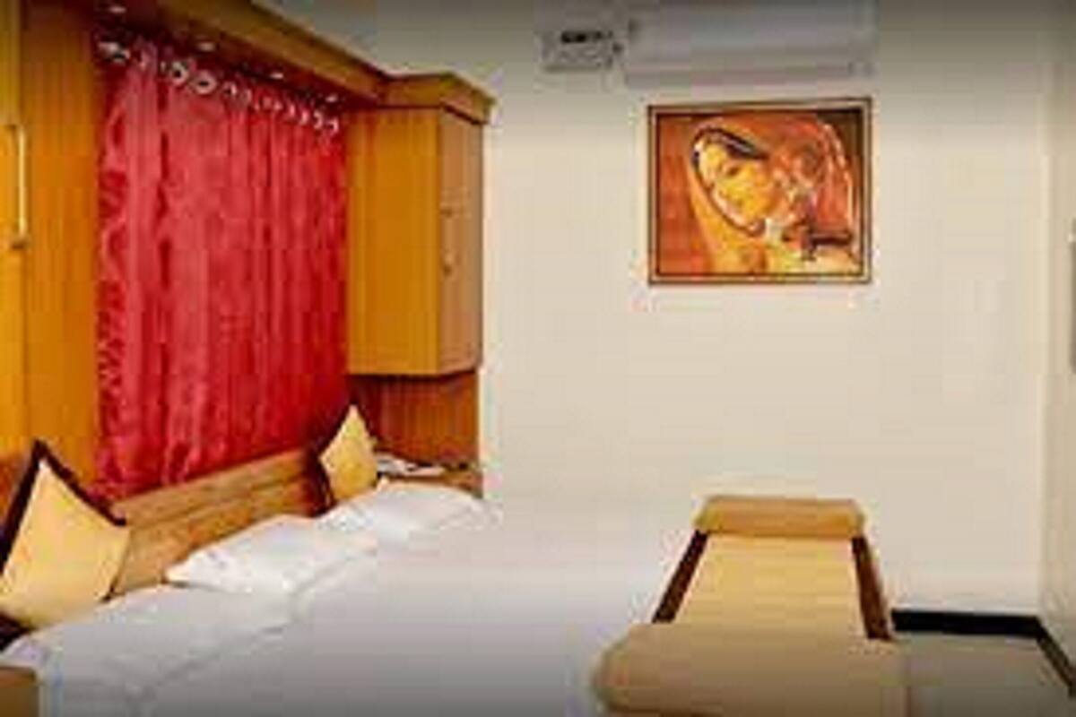 A hotel room with a bed, two bedside tables, a red curtain, and a framed picture on the wall.