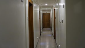 A narrow, well-lit hallway with wooden doors on both sides, leading to a central door at the end. - Anandha Grand (Tiruchendur)