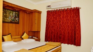 A hotel room with a bed, wooden wardrobe, red curtains, and a painting on the wall. - Anandha Grand (Tiruchendur)