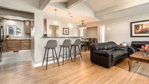 A modern kitchen with wooden cabinets and a dining area with a black leather sofa and bar stools. - D@home Entire &Family by Glenmore Reservoir/Heritage Park/ Rockview Hospital (Calgary)
