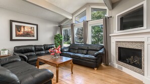 A living room with a sectional sofa, a wooden coffee table with flowers, a fireplace, and large windows. - D@home Entire &Family by Glenmore Reservoir/Heritage Park/ Rockview Hospital (Calgary)