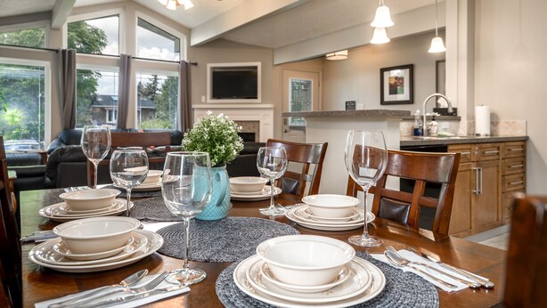 A dining table set for six with white plates, bowls, and cutlery, a blue vase, and a ceiling fan above. - D@home Entire &Family by Glenmore Reservoir/Heritage Park/ Rockview Hospital (Calgary)