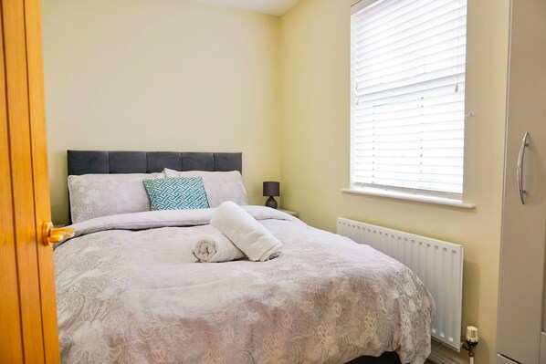 A neatly made bed with a patterned bedspread, a rolled towel, and a decorative pillow. - Clonlum Holiday Cottages (Newry)