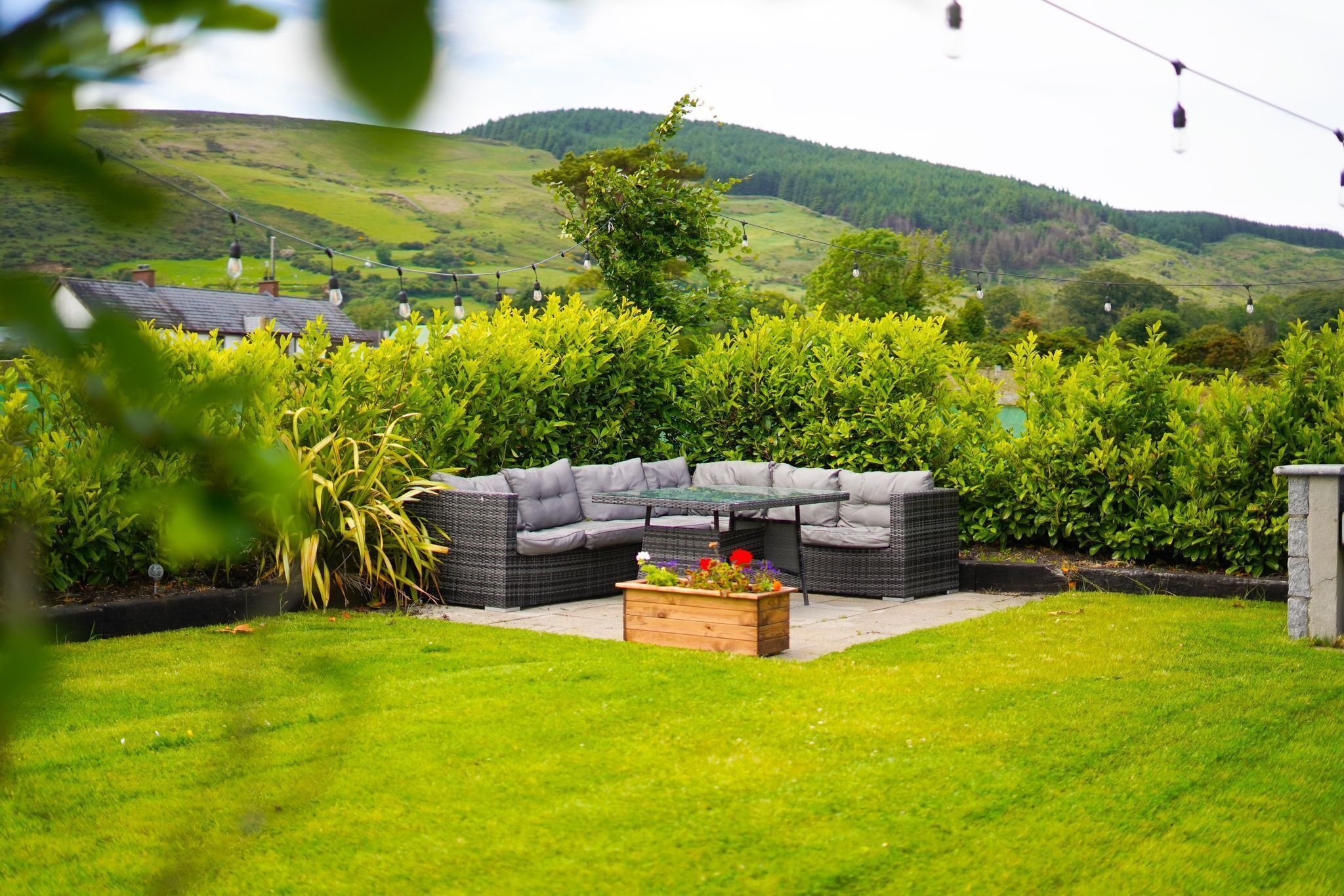 A garden with a curved outdoor seating area, a wooden planter with flowers, and a hedge in the background.