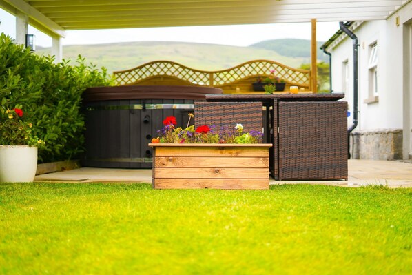A hot tub with a wooden deck and a wicker enclosure, surrounded by a well-maintained lawn and a potted plant.